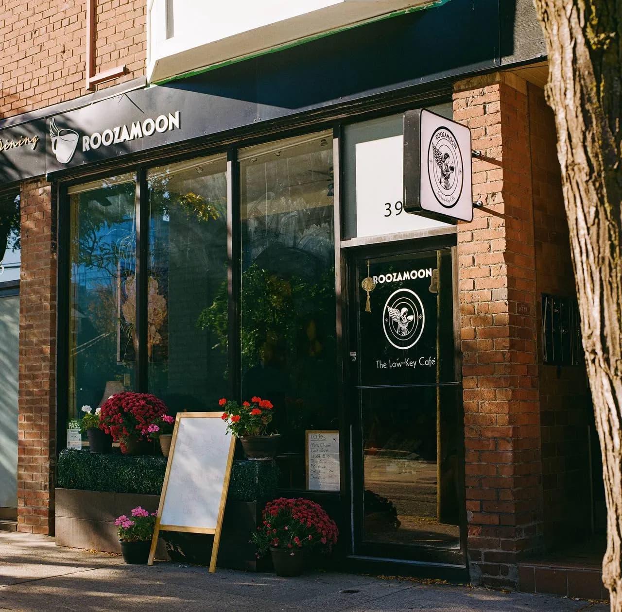 Roozamoon’s storefront in the sun, with flowers and a sandwich board by the window