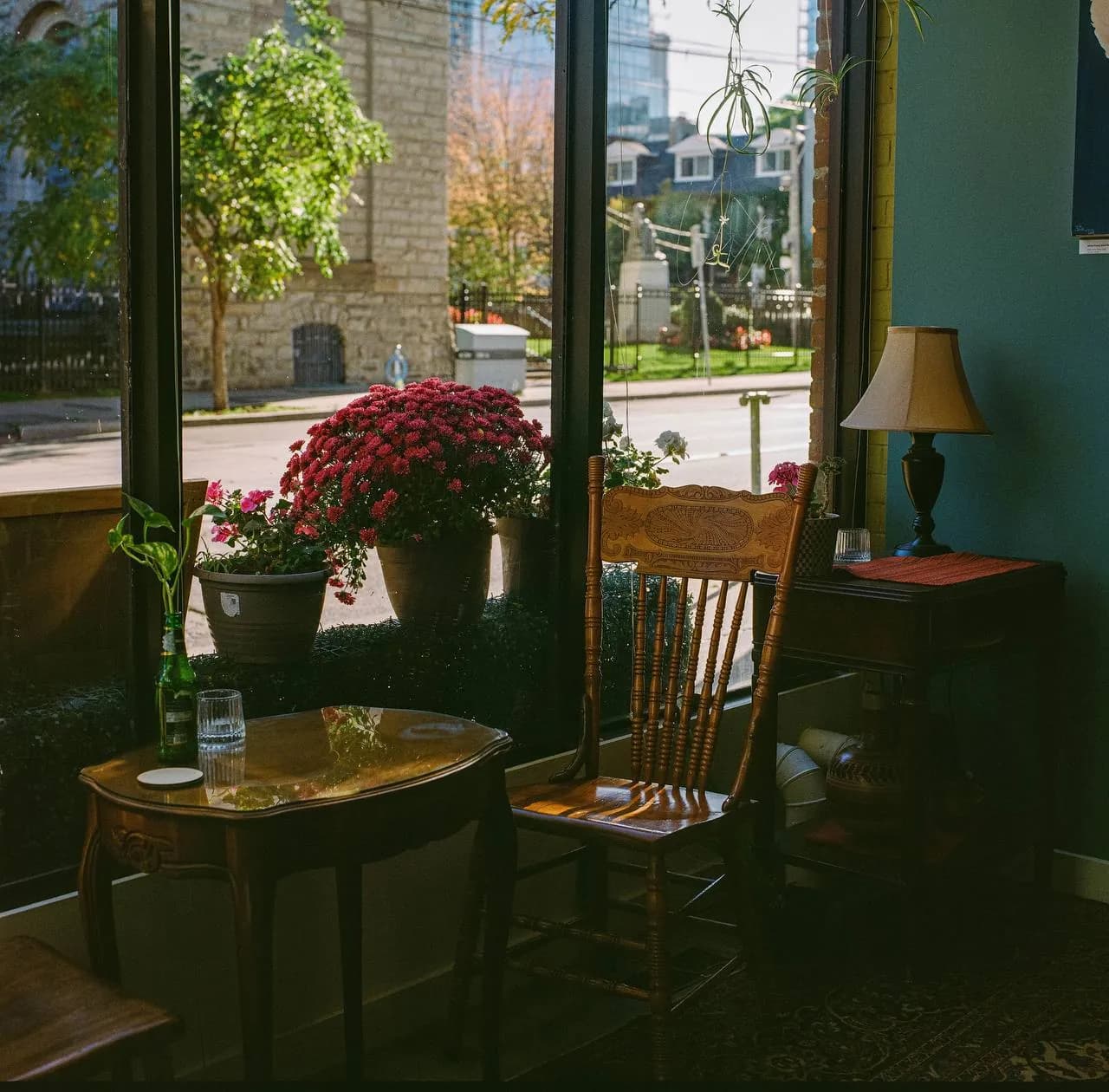 A window table with a wooden chair, red flowers and a lamp, the street outside