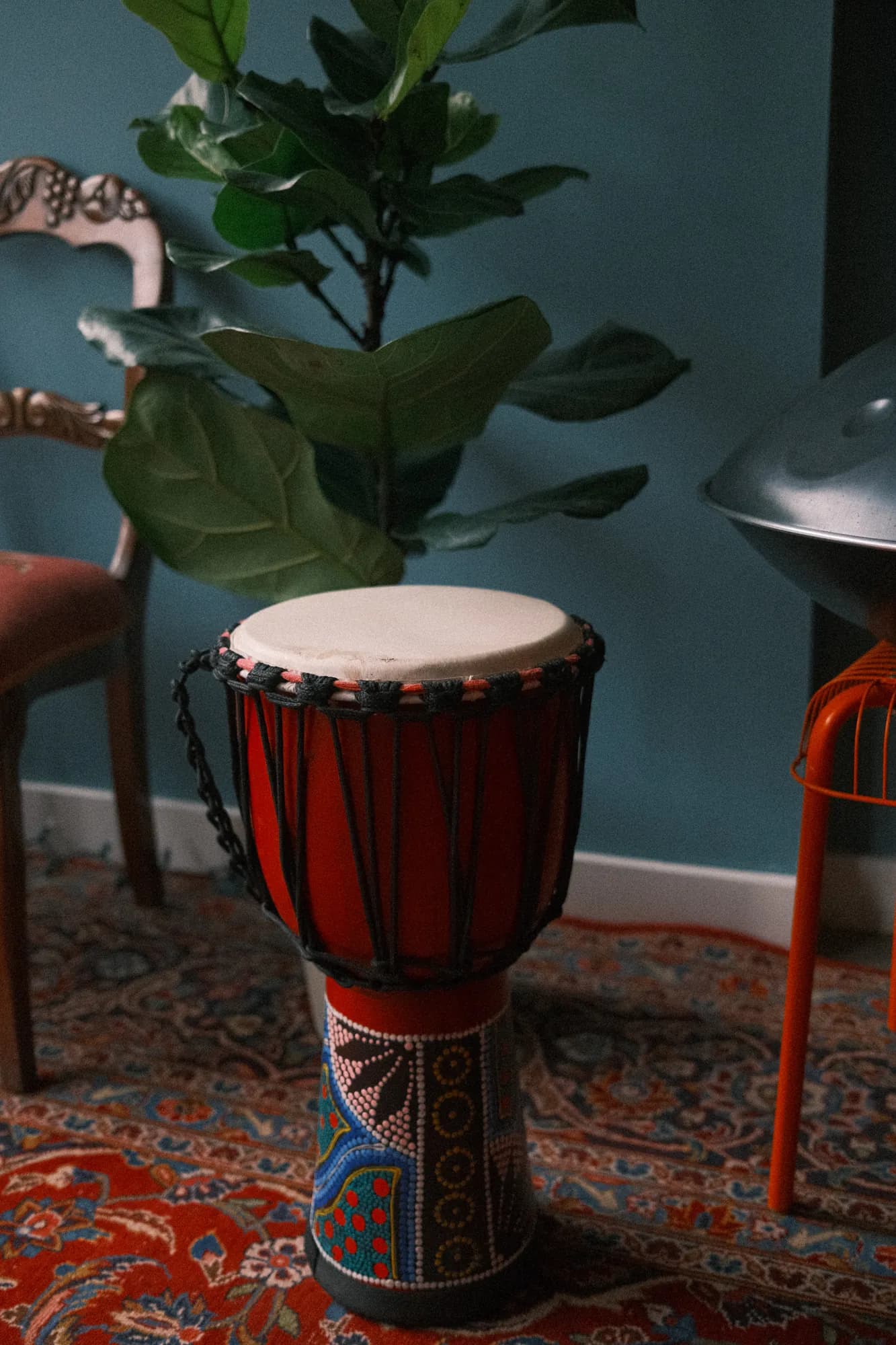 A red hand drum on the Persian rug, a handpan resting on a chair behind it
