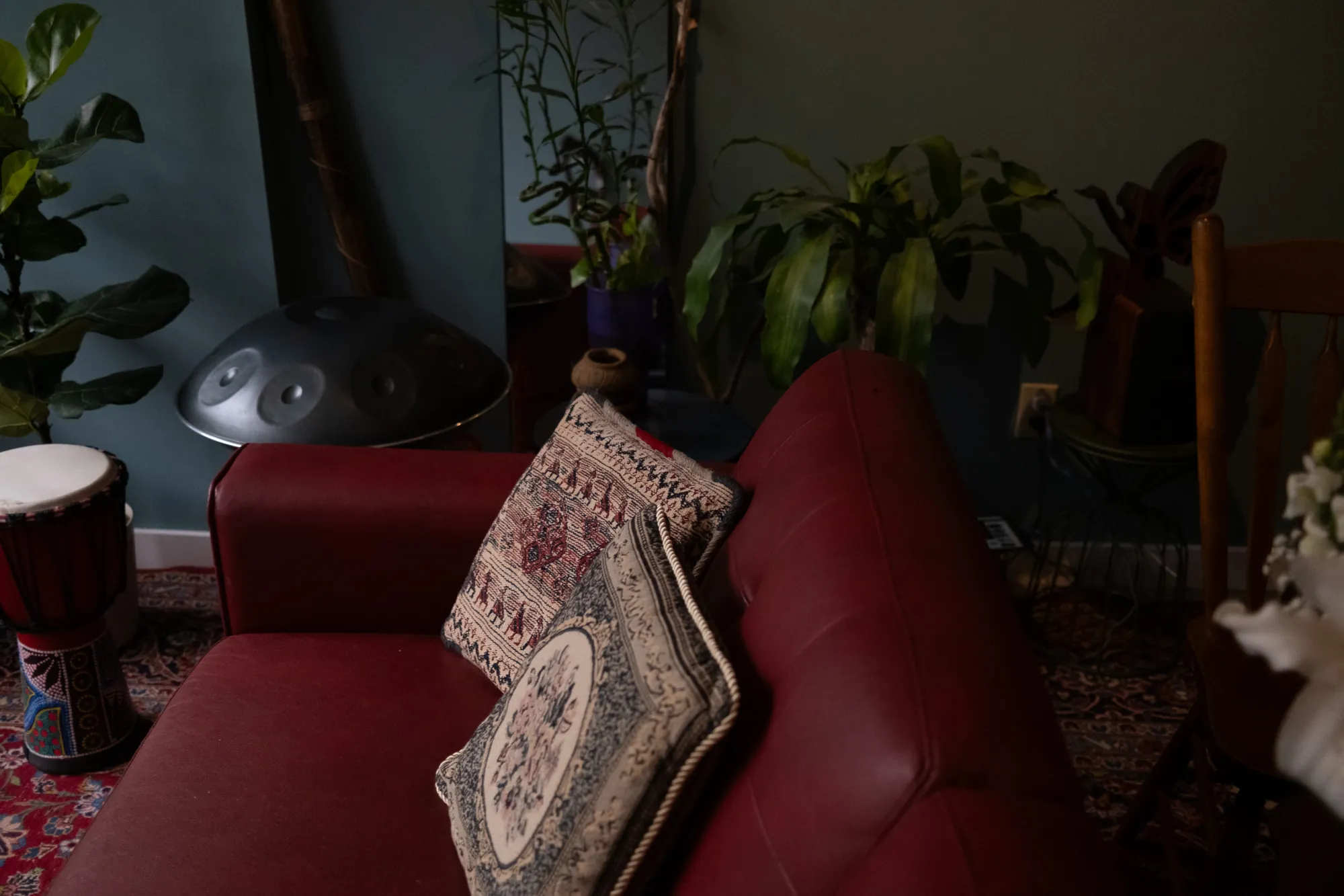 Embroidered cushions on the red sofa, with plants and a handpan behind