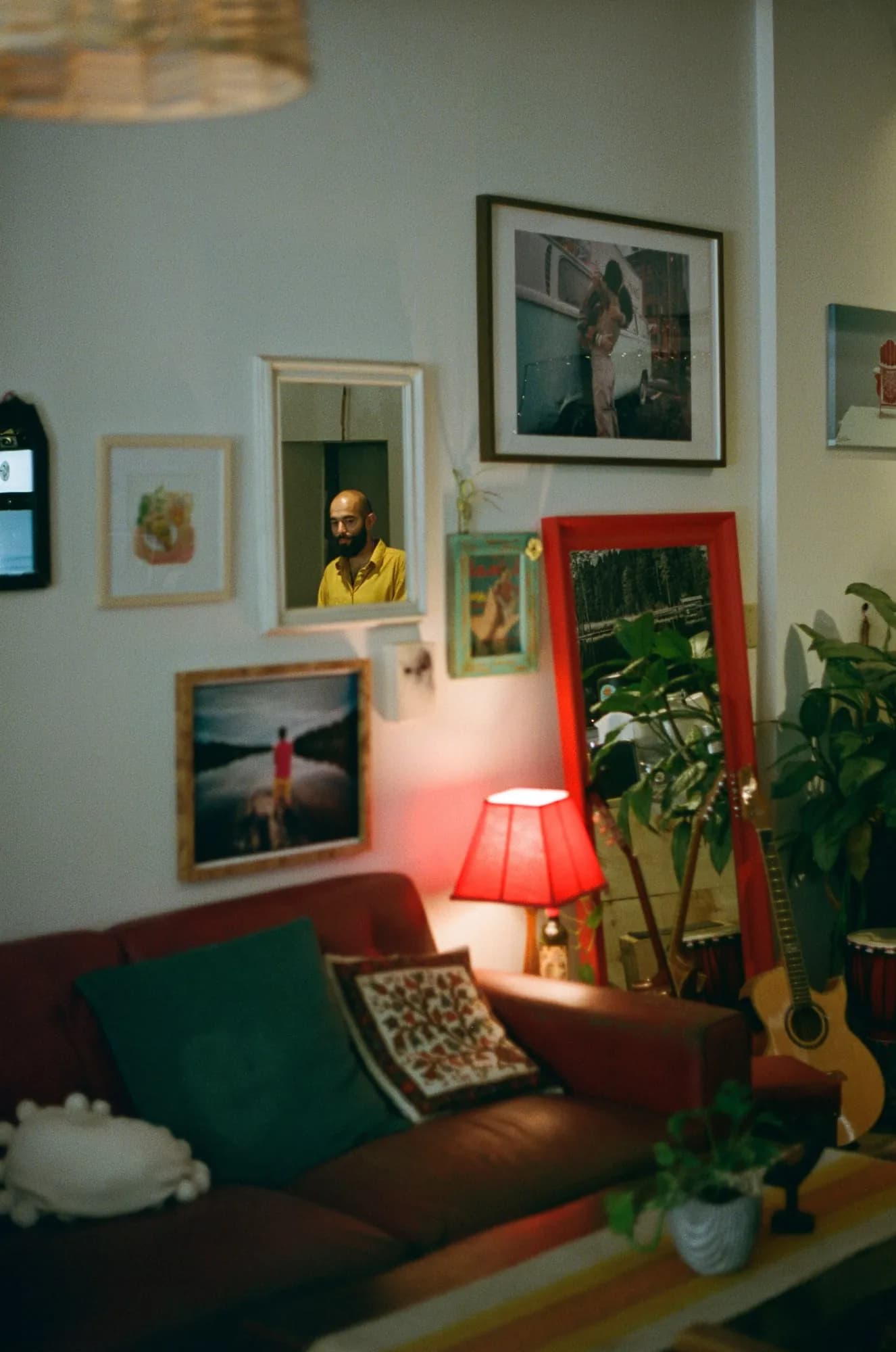 A wall of framed art above the sofa, with a red-framed mirror and a red lamp