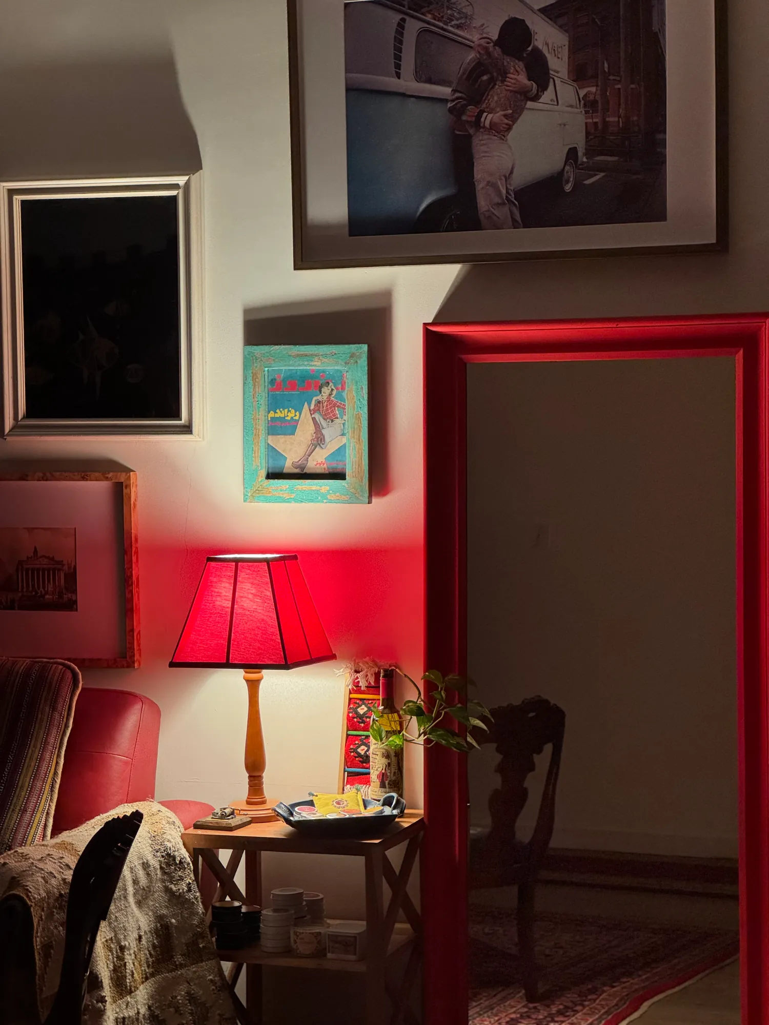 A red lamp glowing beside a red door frame and framed prints